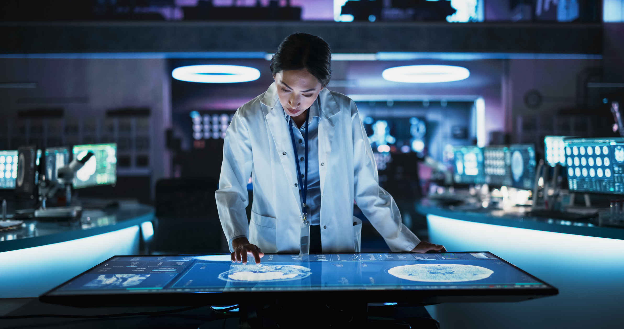 Female Asian Neuroscinetist Using Interactive Touch Screen Table With MRI Scans On Display In Modern Biotechnology Research Center. Doctor Developing Innovative Devices For People With Alzheimer's.